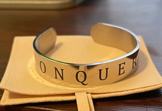 Silver bracelet with 'CONQUEROR' engraving on a beige fabric background Silver bracelet with 'CONQUEROR' engraving on a beige fabric background